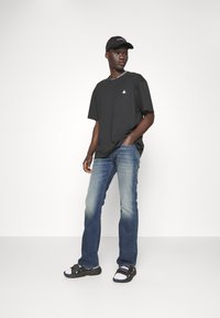 Μαύρο κοντομάνικο μπλουζάκι με εκτύπωση "Λος Άντζελες", συνδυασμένο με ξεθωριασμένα μπλε τζιν και μαύρες σαγιονάρες με λευκές λεπτομέρειες. Ένα μαύρο καπέλο συμπληρώνει την εμφάνιση.