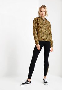 Leopardprint pulloverjack met een halve rits en zwarte leggings. Zwart-witte sneakers, een gladde textuur en een getailleerde silhouet.