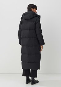 Lange zwarte pufferjas met een capuchon, met een doorgestikt ontwerp en een rechte, getailleerde silhouette; weergegeven van de achterkant, met brede mouwen.