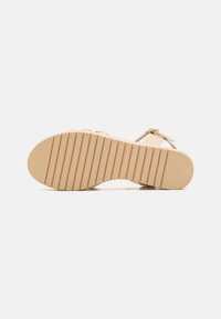 Sandalia beige con una suela de goma texturizada, presenta rayas horizontales para mayor tracción. Diseño minimalista con una única tira y hebilla ajustable.