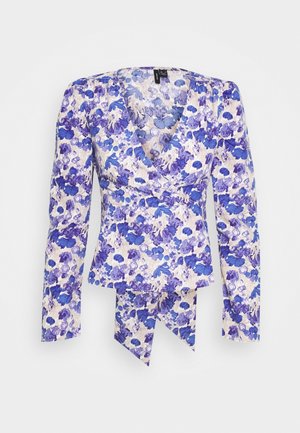 Blusa avvolgente floreale in tessuto bianco con motivi di fiori blu e viola. Presenta maniche lunghe a palloncino e scollatura a V. Dettaglio decorativo con fiocco sull'orlo.