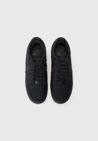 Svarte joggesko med en teksturert stoffoverdel, flate svarte skolisser og gummisåle. Har Nike Air-merke på tungen og siden.