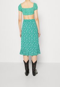 Grøn blomsterprint crop top med pufærmer kombineret med en matchende midilængde nederdel; modellen har sorte cowboystøvler på.