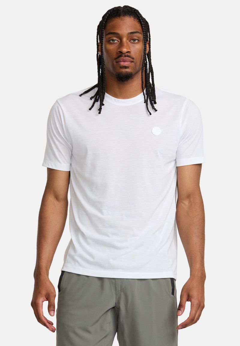 Vit kortärmad t-shirt gjord av lättviktig tyg, med rund halsringning och en liten cirkulär logotyp på vänster bröst.