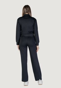 Completo sportivo nero composto da una giacca aderente a maniche lunghe e pantaloni a gamba larga. Tessuto morbido con polsini e vita a costine. Calzature sono sneakers bianche.