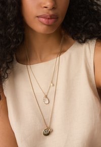 Gold-tone layered necklaces featuring a teardrop pendant with a gemstone, a small pearl, and a circular charm with intricate detailing.