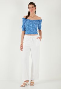 Blå off-shoulder bluse med blomstermønster, parret med hvide vidde bukser; model iført strappy hvide hæle.