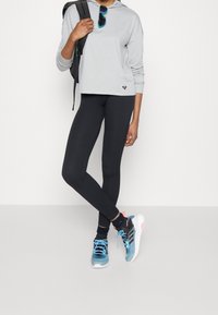 Harmaa pitkähiha tiukka huppari, mustat pinnalliset leggingsit ja siniset lenkkikengät, joissa on vaaleanpunaisia yksityiskohtia. Musta reppu ja aurinkolasit mukana.