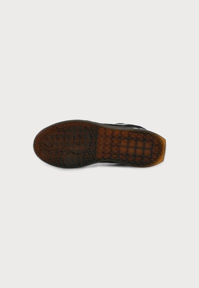 Semelle de chaussure en caoutchouc brun translucide avec des motifs circulaires et en grille texturés sur un fond clair uni.