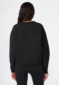Felpa nera con vestibilità rilassata, tessuto testurizzato, spalle cadenti e orlo arrotondato. Abbinata a leggings neri, design minimal.