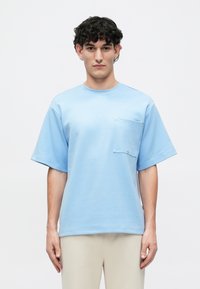 T-shirt de algodão azul claro, com mangas curtas, bolso no peito e detalhes em pressão prateados. Corte descontraído com decote redondo.