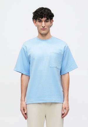 T-shirt azzurro chiaro a maniche corte in cotone con taschino sul petto e dettagli a pressione argentati. Vestibilità comoda con scollatura rotonda.
