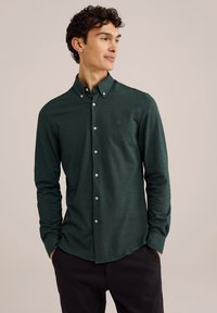 Cămașă verde cu guler, realizată dintr-un material texturat. Prezintă butoane albe și un mic logo pe piept. Design slim fit.