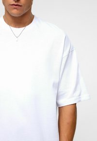 Witte katoenen T-shirt met verlaagde schouders, ronde halslijn en korte mouwen. Kenmerkt zich door een soepele textuur en een losse pasvorm. Zilver kettinghalsketting zichtbaar.