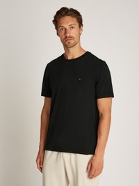 Black cotton t-shirt featuring a crew neckline and short sleeves, with a small embroidered logo on the chest, paired with light grey sweatpants.