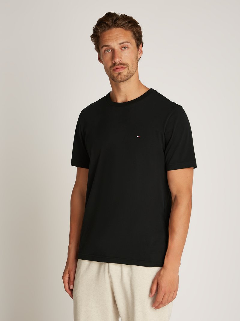 Black cotton t-shirt featuring a crew neckline and short sleeves, with a small embroidered logo on the chest, paired with light grey sweatpants.