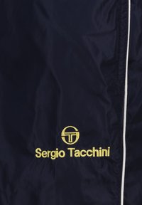 Giacca a vento navy con una texture liscia, caratterizzata da un logo ricamato giallo "Sergio Tacchini" e un accento circolare, rifinita in bianco.