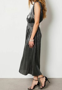 Metallic svart midikjol med veckad textur, åtsittande midja och ärmlös design. Matchas med svarta remförsedda högklackade sandaler.