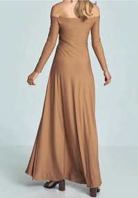 Ruskea off-the-shoulder, pitkähihainen mekko, joka on valmistettu sileästä kankaasta ja sisältää lattiaan asti ulottuvan helman sekä tiukan yläosan. Litteät sandaalit täydentävät asun.