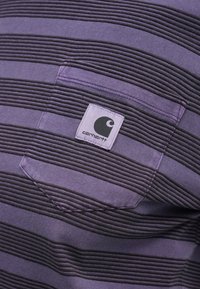 Purpurna črtasta majica z teksturiranim vzorcem, z kontrastno žepno, ki prikazuje logotip v zgornjem levem kotu.