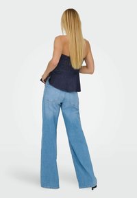 Denim brezramni top z nabranim korpusom, kombiniran z svetloblue širokimi hlačami. Gladka tekstura in sproščen kroj povečujeta udobje.