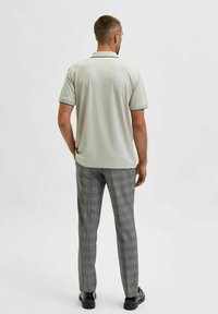 Polo shirt gris clair avec un col contrastant, associé à un pantalon à carreaux gris. Les matériaux semblent lisses avec une coupe ajustée.