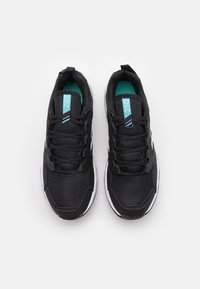 Zapatillas deportivas negras con un upper de malla texturizada, detalles en turquesa y suelas blancas. Cuenta con un diseño de cordones y una etiqueta de marca prominente.