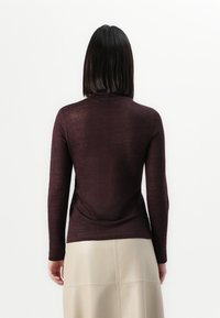 Haut bordeaux à manches longues, ajusté, en tissu doux et léger, avec un col rond et une texture subtile, associé à une jupe midi beige.