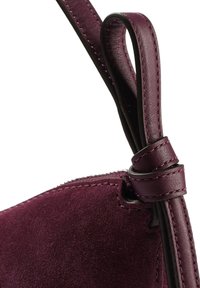 Borsa in suede bordeaux con tracolla in pelle liscia. Presenta un dettaglio annodato e cuciture lungo i bordi.
