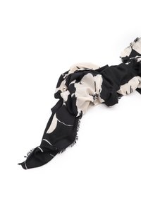 Sciarpa nera e crema con motivi floreali astratti, realizzata in materiale morbido con bordi frangiati, drappeggiata elegantemente.