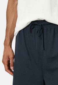 Marineblaue Shorts mit elastischem Bund und Kordelzug. Hergestellt aus weichem Stoff, mit Seitentaschen. Kombiniert mit einem hellen Oberteil.