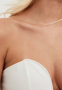 Top strapless blanco con textura suave y diseño estructurado, que presenta un escote amplio y bordes limpios, situado sobre un fondo neutro.