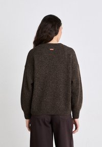 Bruin gebreid trui met een losse pasvorm, verlaagde schouders, geribbelde manchetten en zoom, met een klein roze label aan de achterkant van de halslijn.