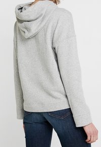 Felpa grigia con cappuccio e fitting rilassato, dotata di tasca a marsupio e polsini a costine, abbinata a jeans blu scuro.