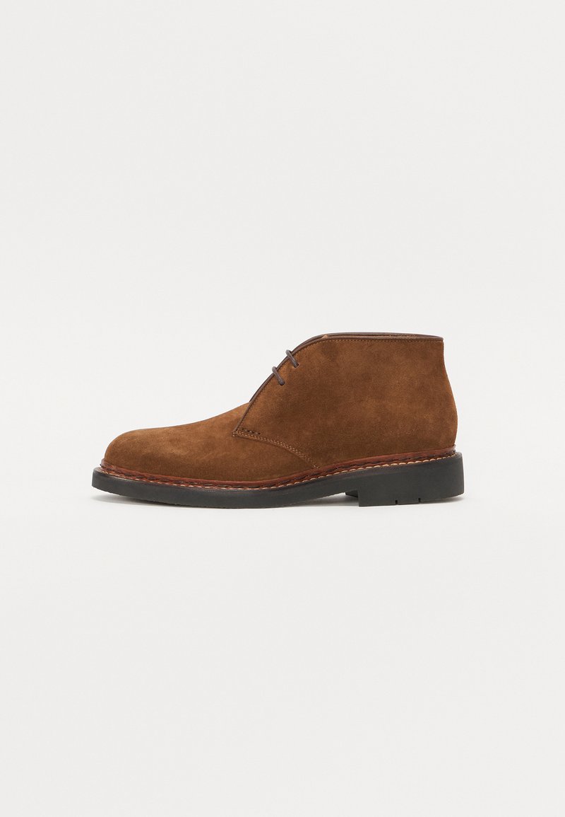 Bruine suède chukka-boten met een ronde neus, minimale stikdetails en een zwarte rubberen zool, voorzien van twee oogjes voor veters.