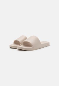 Beige Gummisandalen mit breitem, offenem Riemen und strukturiertem Fußbett. Flache Sohle ohne sichtbare Beschläge oder Muster.