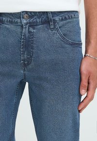 Blauwe denim jeans met een nauwsluitende pasvorm, voorzien van een knoopsluiting en voorzakken. De stof heeft een gladde textuur en een lichte vervaging.