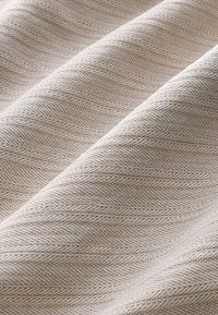 Tissu texturé beige clair avec un motif en chevrons, présentant des drapés ondulés qui mettent en valeur la douceur du matériau et les détails du tissage.