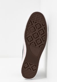 Semelle d'une basket Converse noir et blanc montrant un motif de bande de roulement marron détaillé et le logo sur un fond blanc.