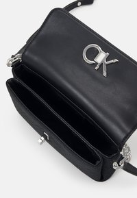 Borsa a tracolla in pelle nera con finitura texture, hardware argentato e dettaglio del logo sulla patta. Presenta due scomparti interni.