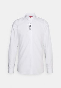 Witte lange mouwen shirt van katoen, met een puntige kraag en een verticale zwarte logo-detail aan de voorkant. Glad textuur.