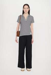 Ribaga polo särk tumesinises ja valges, kraega, koos lõdva mustade pükstega ja kreemivärvi kingadega. Lisandid hõlmavad pruuni ristiõlal kotti.