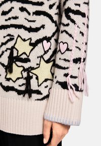 Strickpullover mit weicher rosa Grundfarbe, schwarzen und cremefarbenen Streifen sowie bunten Stern- und Herzapplikationen mit rosa Quasten am Ärmel.