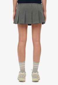 Grijs gestreepte rok met plooien, casual design, gecombineerd met beige sneakers en grijs gestreepte sokken. Achteraanzicht, waarin de zoom van de rok zichtbaar is.