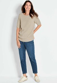 Lichtbeige gebreide trui met korte mouwen, ronde halslijn en ribbelrand, gecombineerd met donkerblauwe jeans en lichte sneakers.