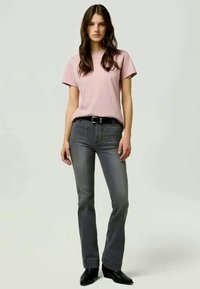 Light pink short-sleeve t-shirt paired with dark grey bootcut jeans, featuring a black belt and sleek black ankle boots.