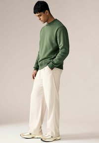 Groene sweatshirt met een ronde halslijn, gecombineerd met losse crèmekleurige broeken en beige sneakers met zwarte accenten.