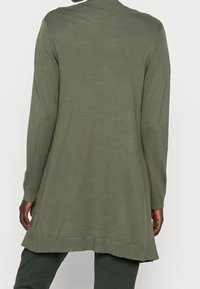 Langærmet, olivengrøn strikket top med ribbet krave. Har sideslidser ved kanten og tekstureret stof. Blødt, let materiale.