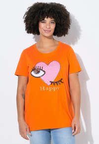 Orange bomulds t-shirt med et grafisk motiv af et pink hjerte og øje. Teksten "Happy" i metallisk sølv. Casual fit med korte ærmer.