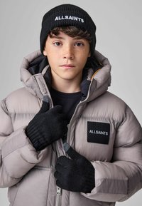 Nafoukaná světle šedá bunda s černou nášivkou označenou "ALLSAINTS", černá žebrovaná čepice a černé pletené rukavice se šedými akcenty.